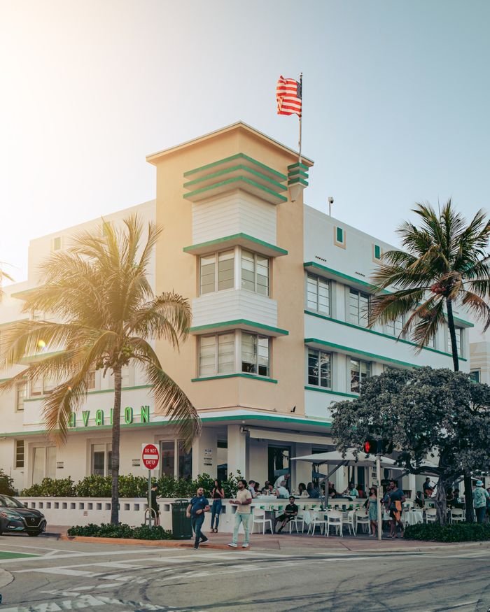 Crafting Captivating Headlines: Your awesome post title goes here Art Deco building with palm trees and American flag in sunny Miami Beach intersection.